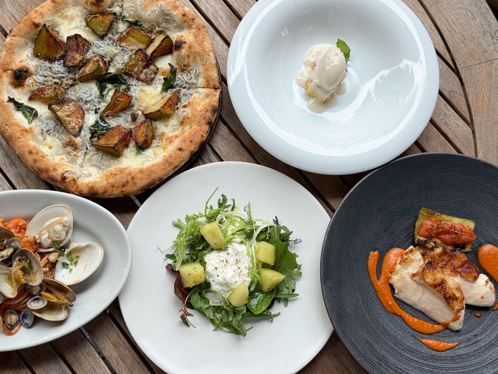 A spread at MORETHAN: wood-fired pizza, vongole, burrata salad, and grilled chicken